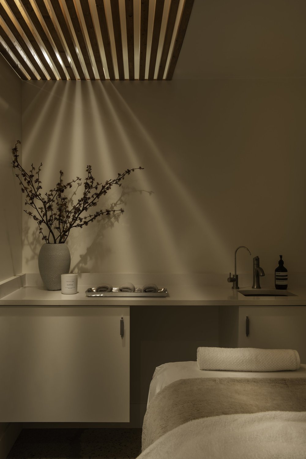 Skin Wellness Boutique — Treatment room with a bed, cabinetry and timber ceiling slats casting patterned light