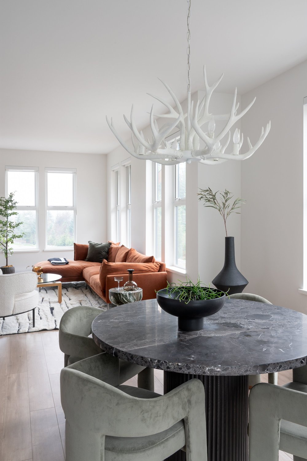 Britannia Beach House — Dining table and green upholstered chairs beneath a branching white light fixture