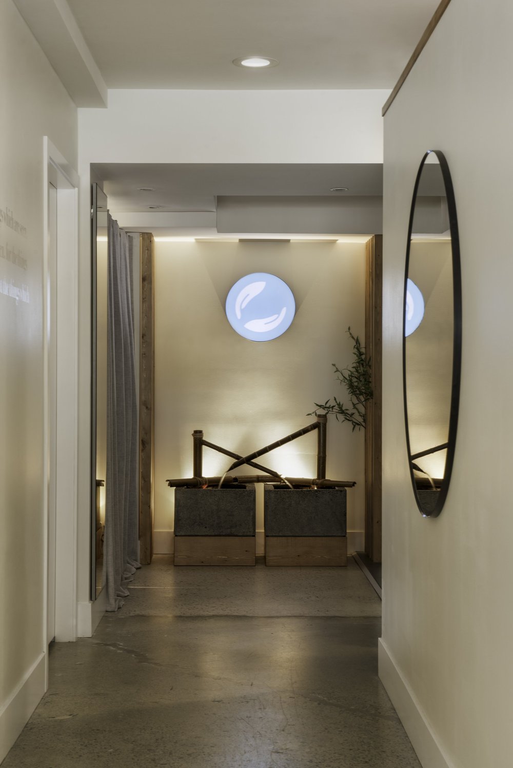 Skin Wellness Boutique — Narrow passage with circular mirror and fountain at its end