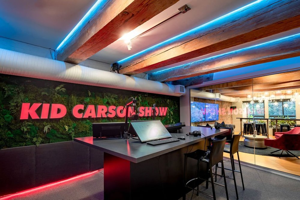 Podcast Studio — Recording desk behind glass with blue ceiling lighting and Kid Carson signage
