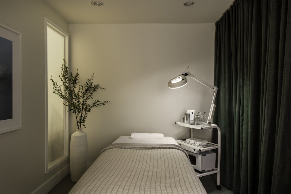 Skin Wellness Boutique — Treatment bed beside a task lamp and dark curtain