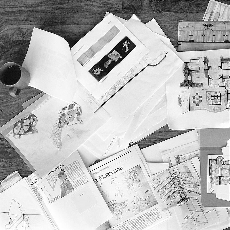 Overhead black-and-white view of design books, photographs and drawings on a studio table